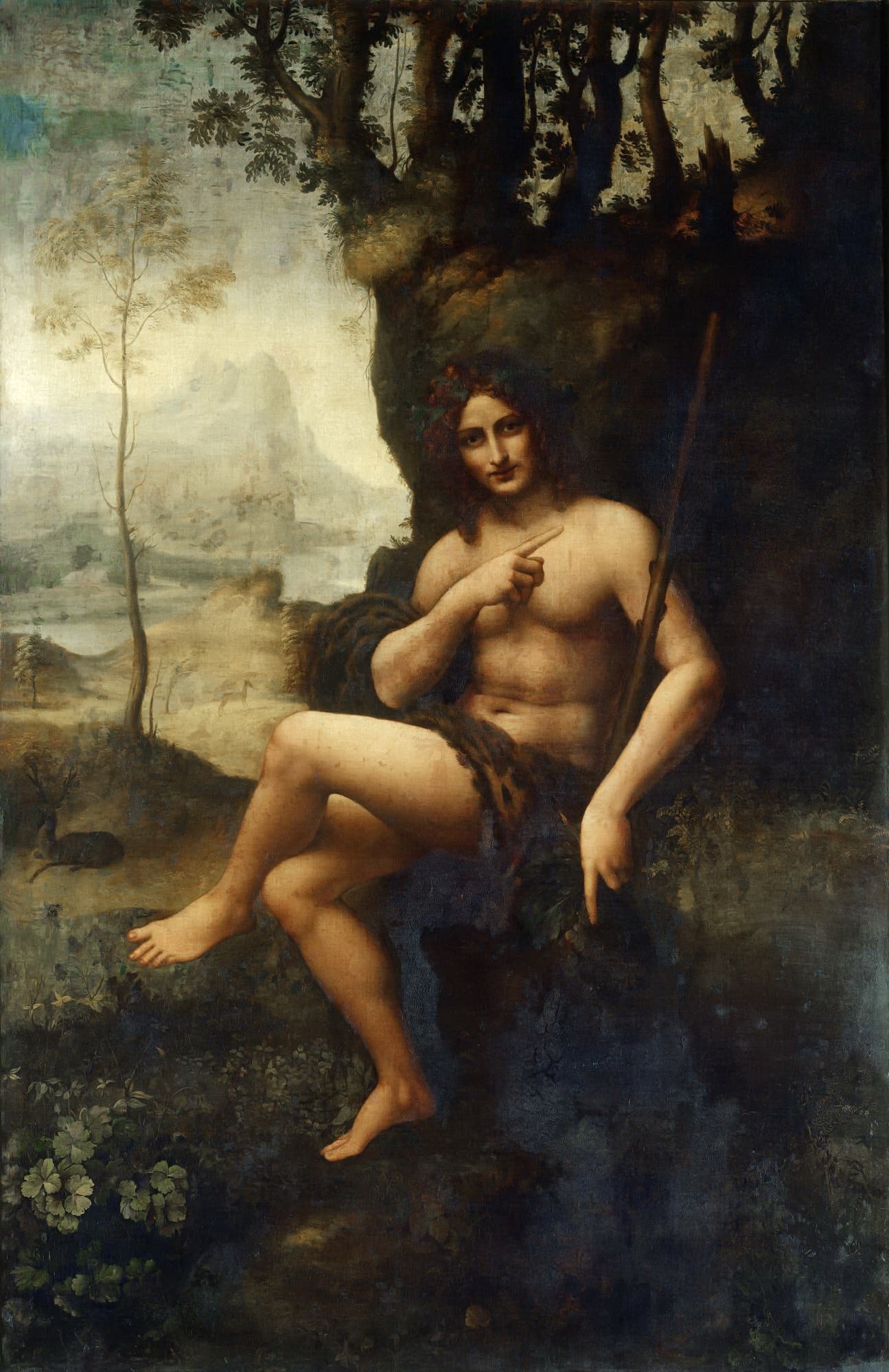 A nude young man crowned with vine leaves sits on a rock beside a wood, pointing across his chest and down to the ground, with a misty mountain landscape behind — Workshop of Leonardo da Vinci, Bacchus (Saint John the Baptist), c. 1510–15