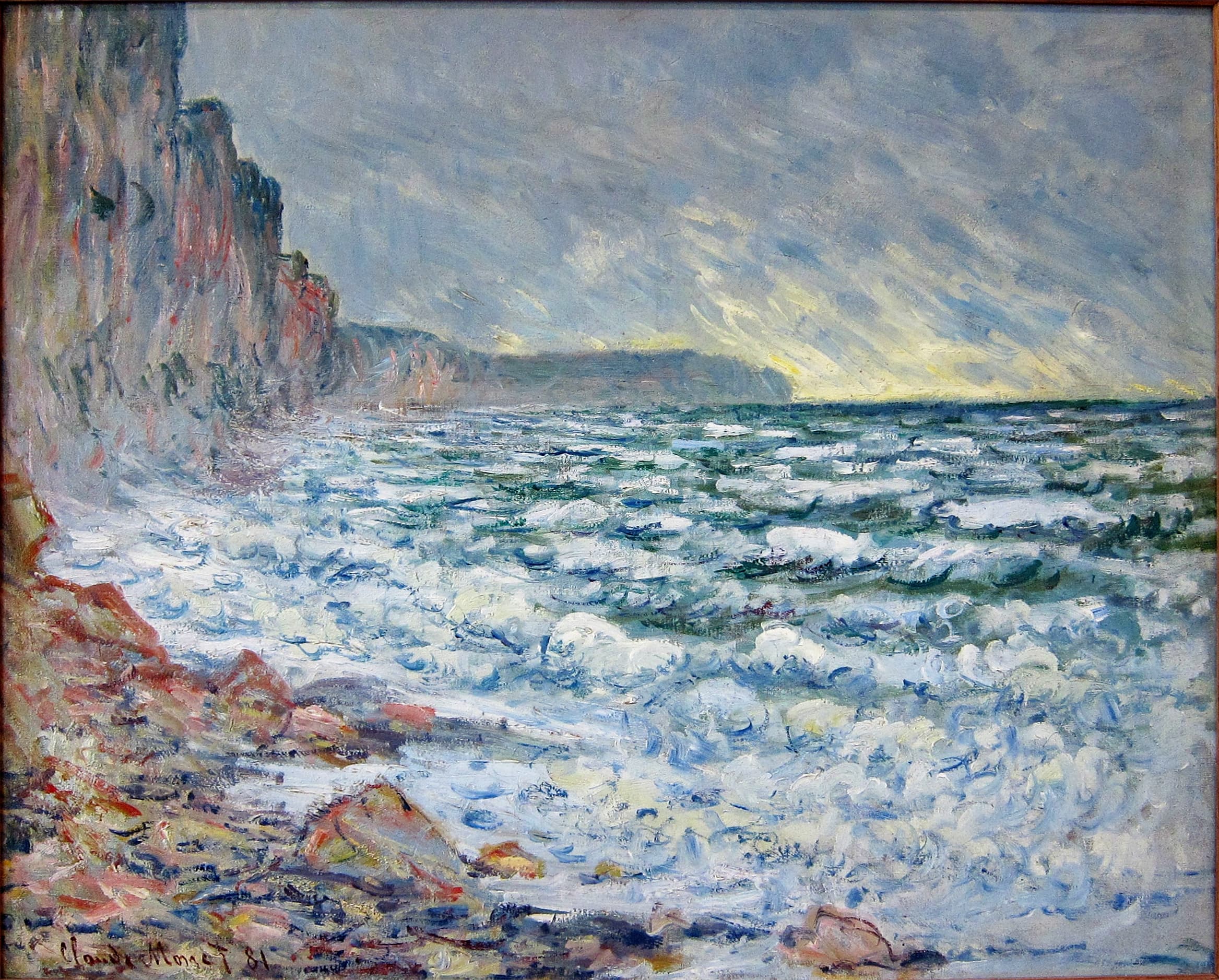 A rough gray-blue sea breaks on rocky shingle below a tall chalk cliff at left, a rainy sky opening to yellow light — Claude Monet, Fécamp, by the Sea, 1881