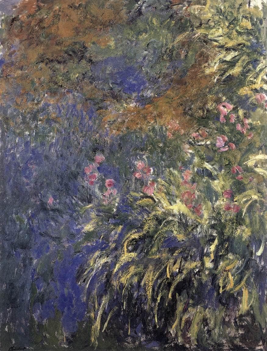 Long yellow-green iris leaves arch across the canvas among pink and mauve blooms beside blue-violet pond water, with rust-colored foliage at the top — Claude Monet, Irises by the Pond, c. 1914–17