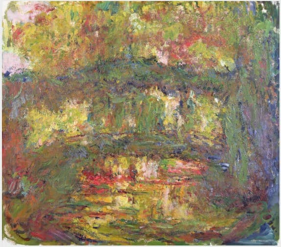 A low olive arch beneath sunlit gold and green foliage, willow fronds hanging under it and reflected in yellow and coral strokes on the pond — Claude Monet, Le pont japonais, c. 1918–24