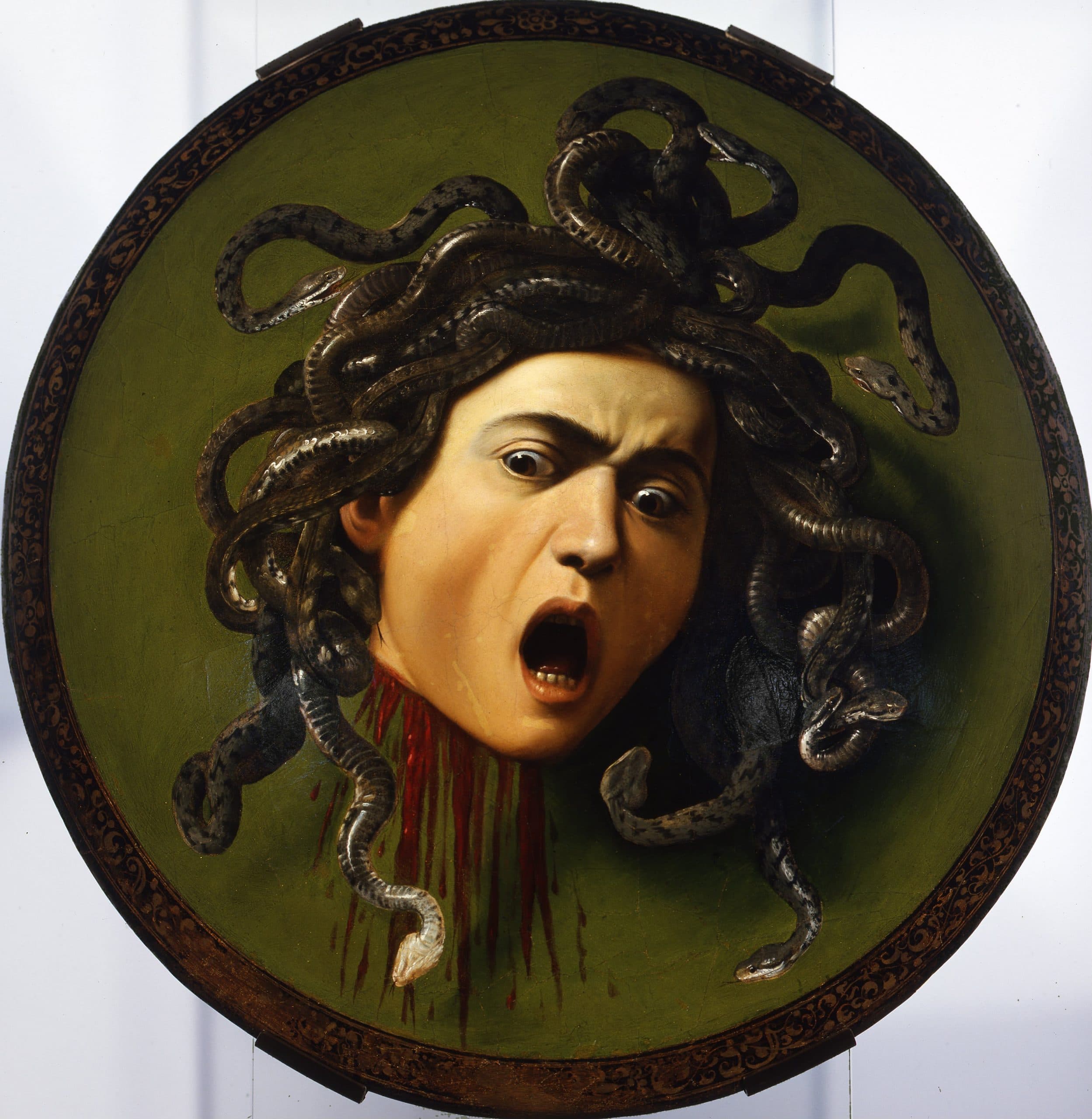 A screaming severed head with wild eyes and writhing snakes for hair, blood streaming from its neck, painted on a round green shield — Caravaggio, Medusa, c. 1597–98