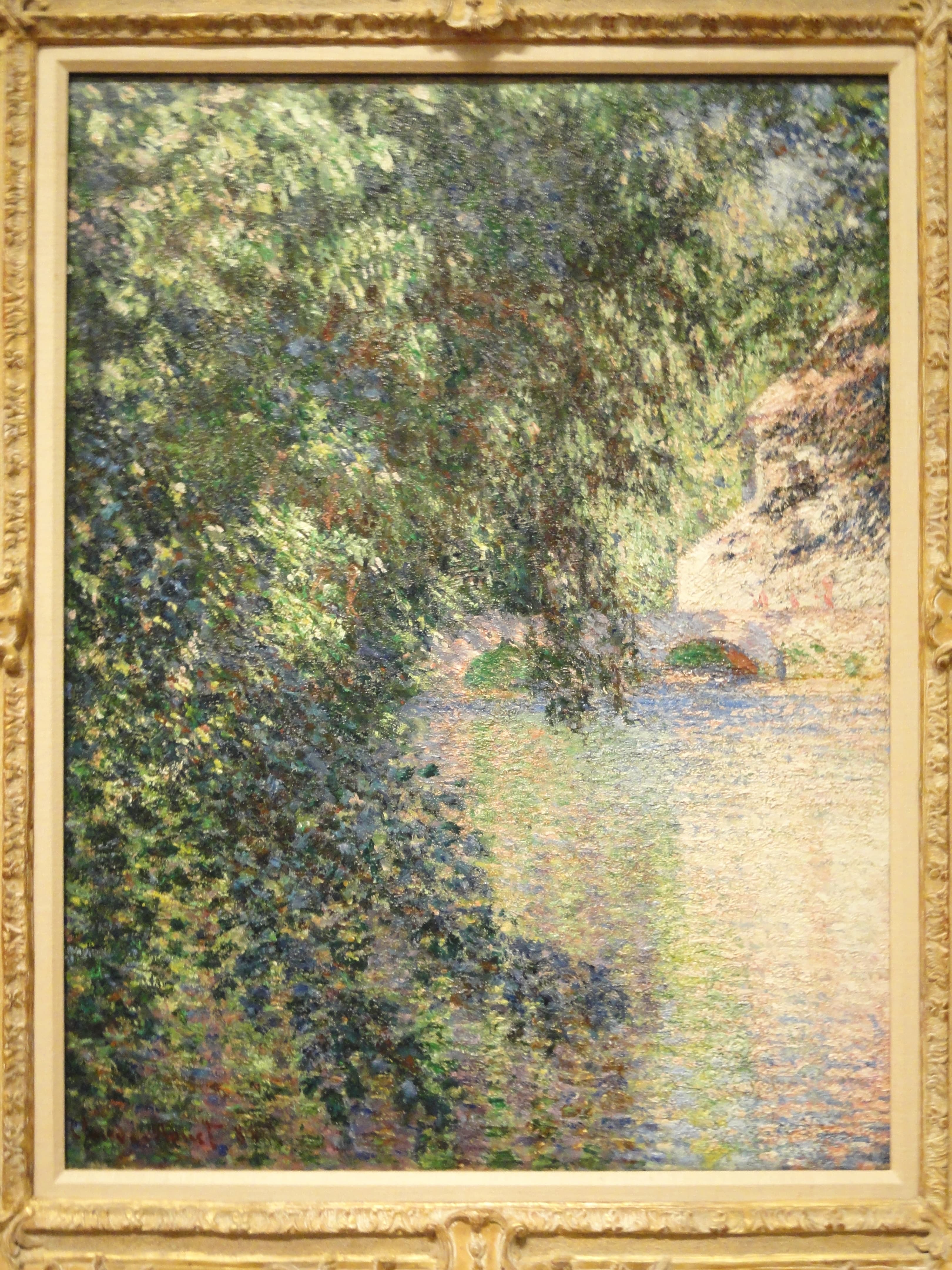A curtain of green summer foliage hangs over a pale, glowing river channel, with a small mill and arched bridge far off at the end — Claude Monet, Mill at Limetz, 1888