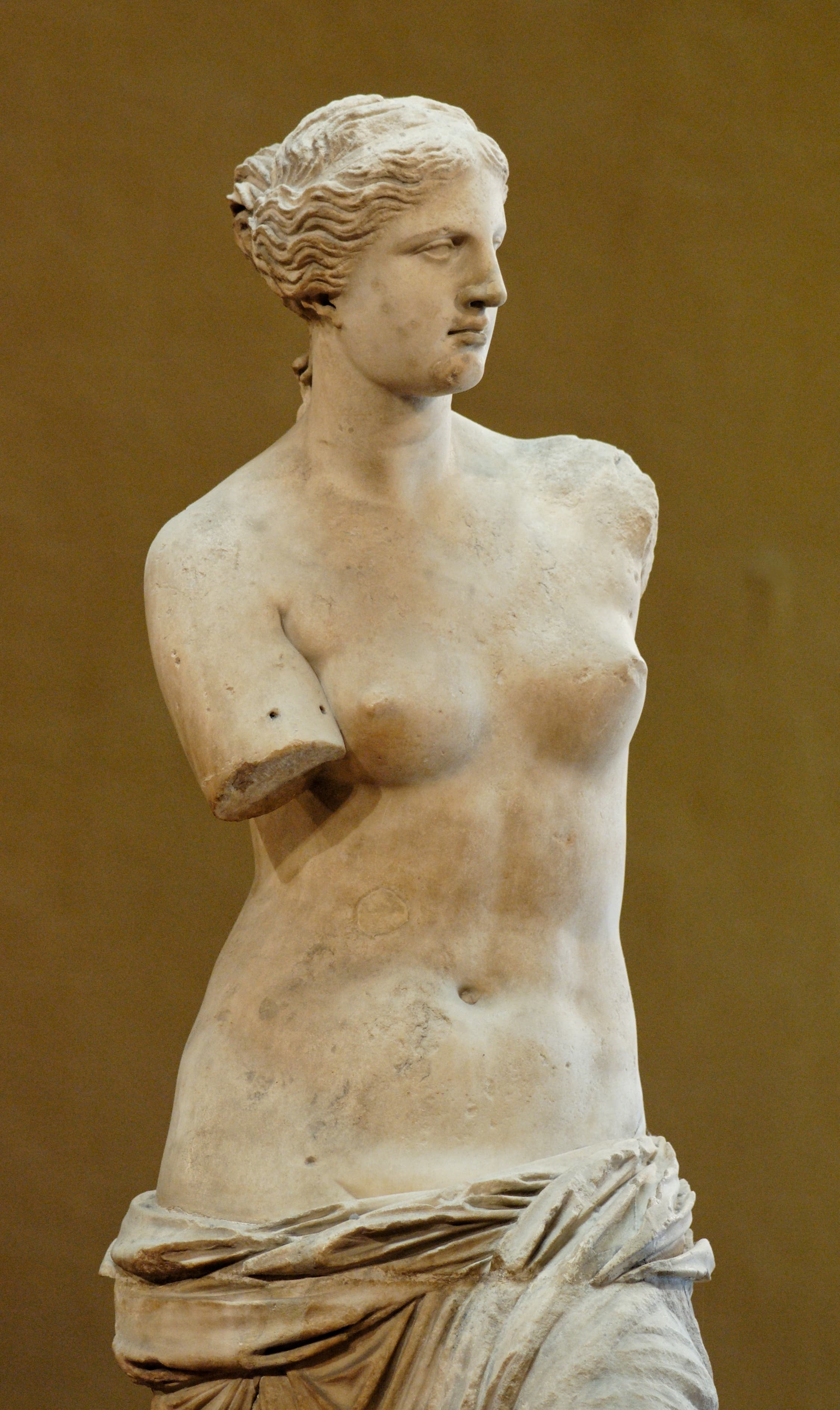 An armless marble statue of a half-nude goddess with drapery slipping from her hips, her head turned to the side — Alexandros of Antioch, Venus de Milo, c. 150–125 BC, Louvre