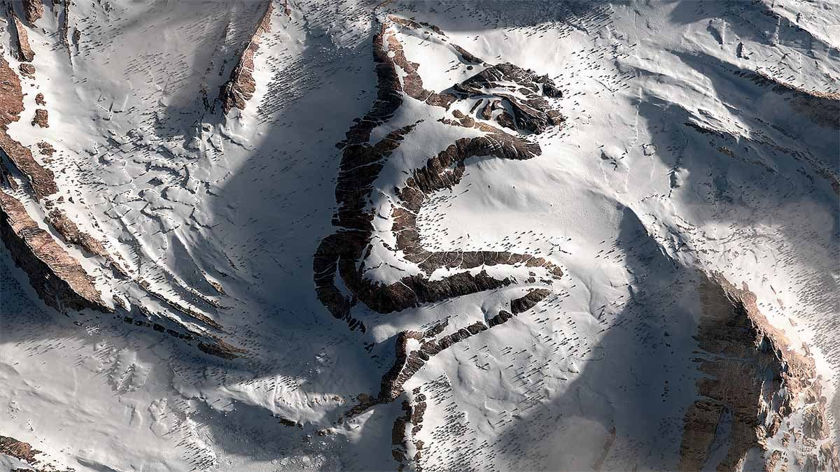 Seen from above, ridges of dark rock in a snowy mountainside form the outline of a woman lying asleep — Jean-Michel Bihorel, Winter Sleep, 2020