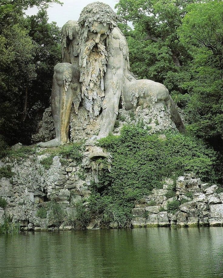 A colossal bearded stone giant crouches on a rocky outcrop above a still pond, moss and trees around him — Giambologna, Apennine Colossus, c. 1579–80