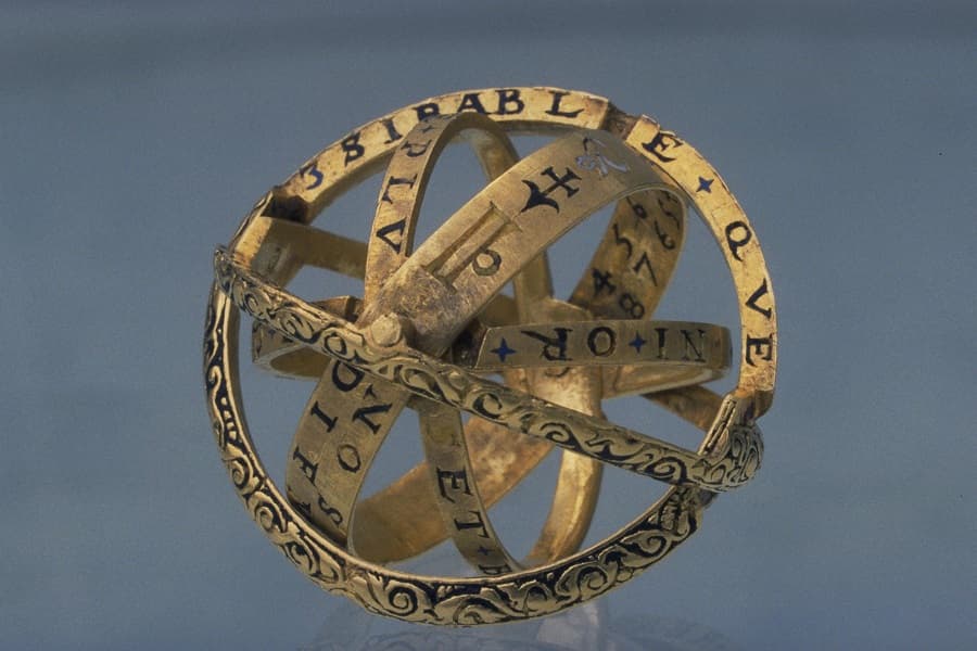 A gold ring opened into a small sphere of crossing bands decorated with scrolls, stars and enameled lettering — an armillary sphere ring