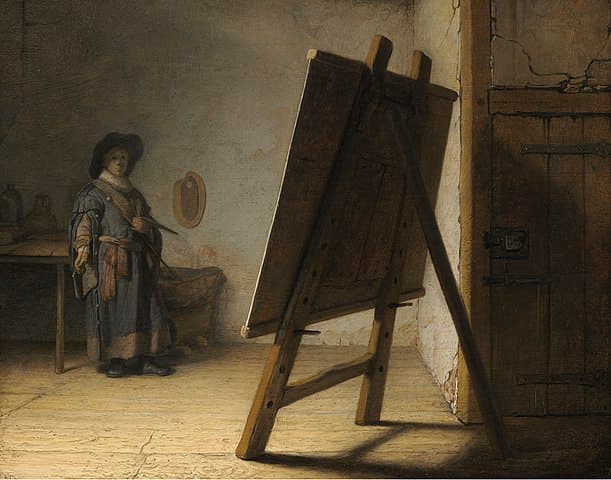 A small painter in a hat and smock stands at the back of a bare studio, facing a large easel seen from behind in the foreground — Rembrandt, The Artist in His Studio, c. 1628