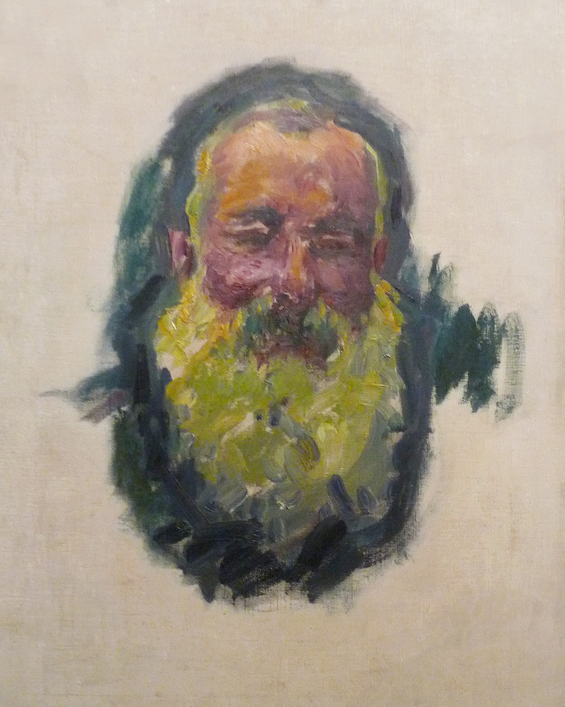 An old man's ruddy face with a full beard painted in yellow-green and cream strokes, floating on bare pale canvas inside a dark blue-green halo — Claude Monet, Self-Portrait, 1917