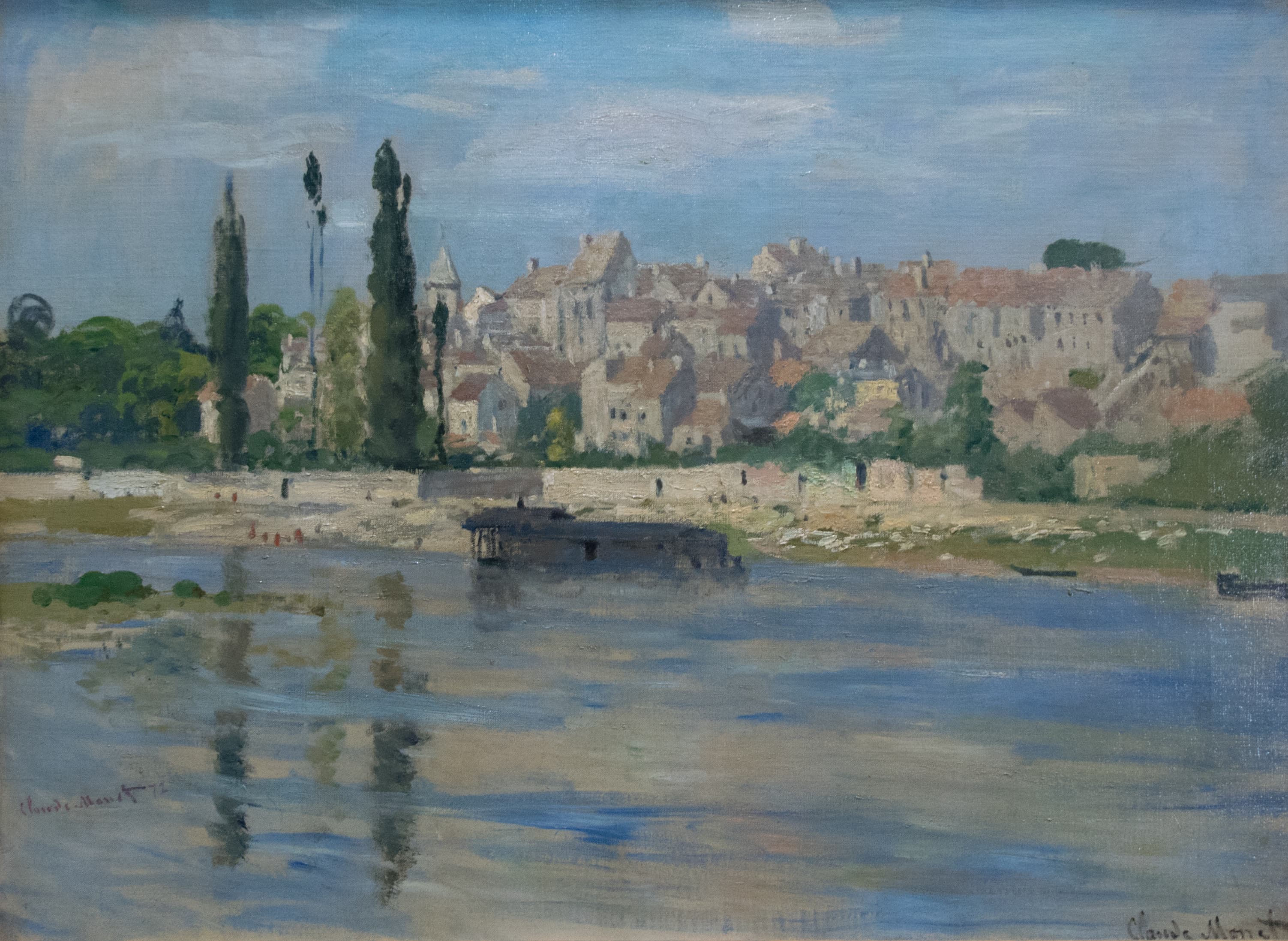 A village of pale houses with a church spire and tall poplars rises above a stone wall along a calm blue river, reflections below — Claude Monet, Carrières-Saint-Denis, 1872