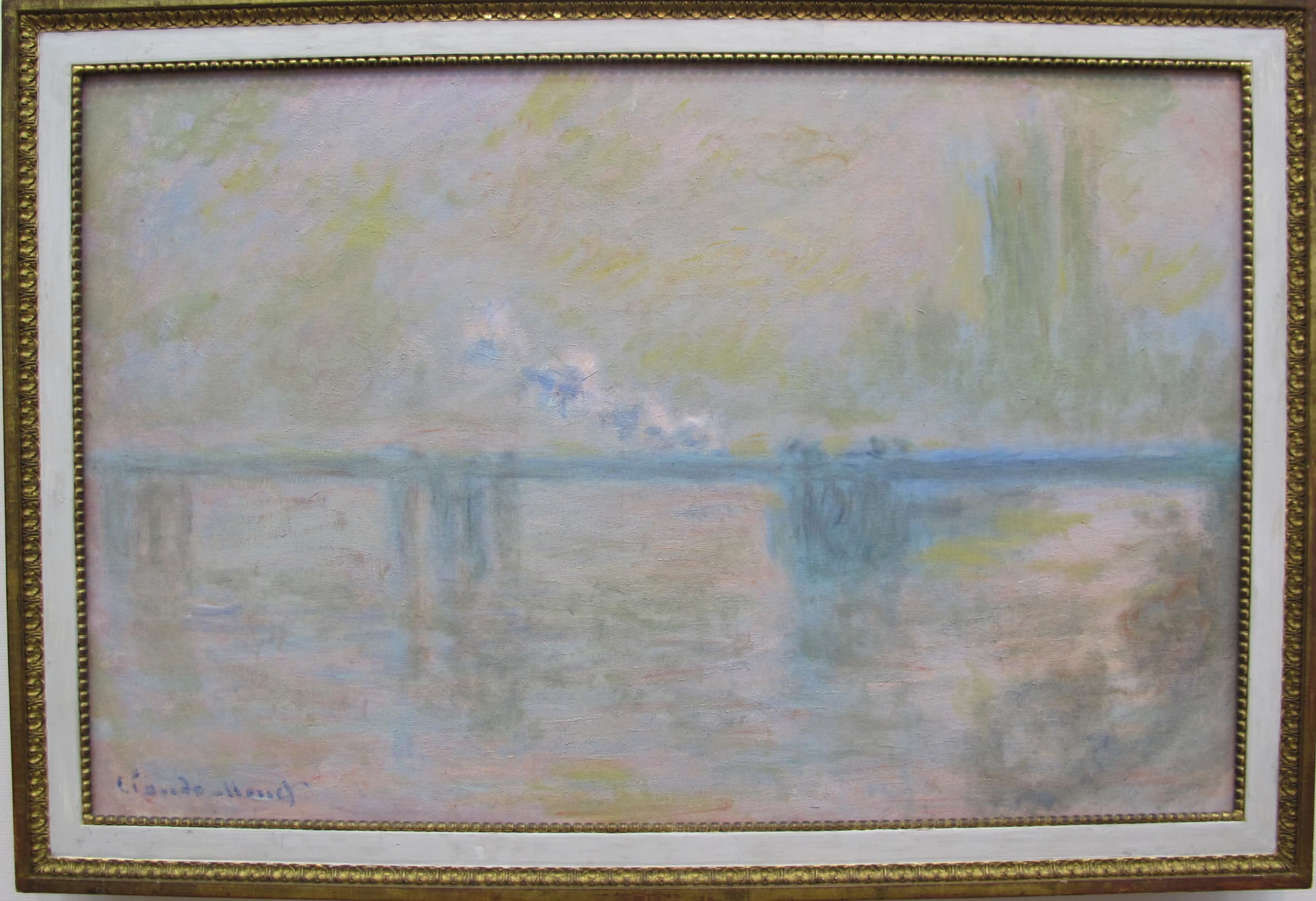 A pale turquoise bridge crosses a river in soft pink and yellow haze, Parliament's towers faint at right, shown in a gilt frame — Claude Monet, Charing Cross Bridge (Overcast Day), 1900