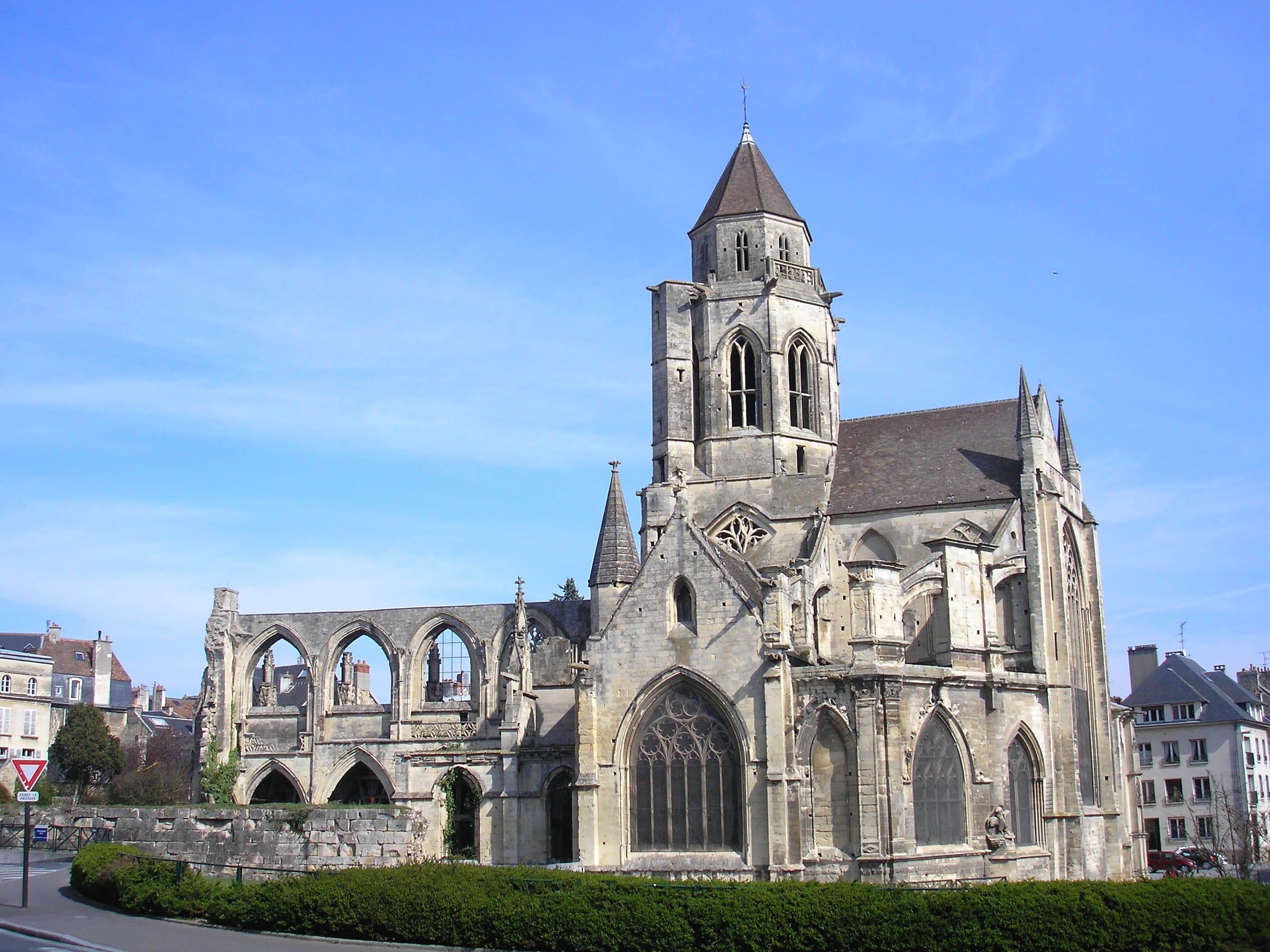 A weathered Gothic church with a square crossing tower and slate spire, its roofless nave arcade open to the sky at the left — Church of Saint-Étienne-le-Vieux, Caen, 15th century