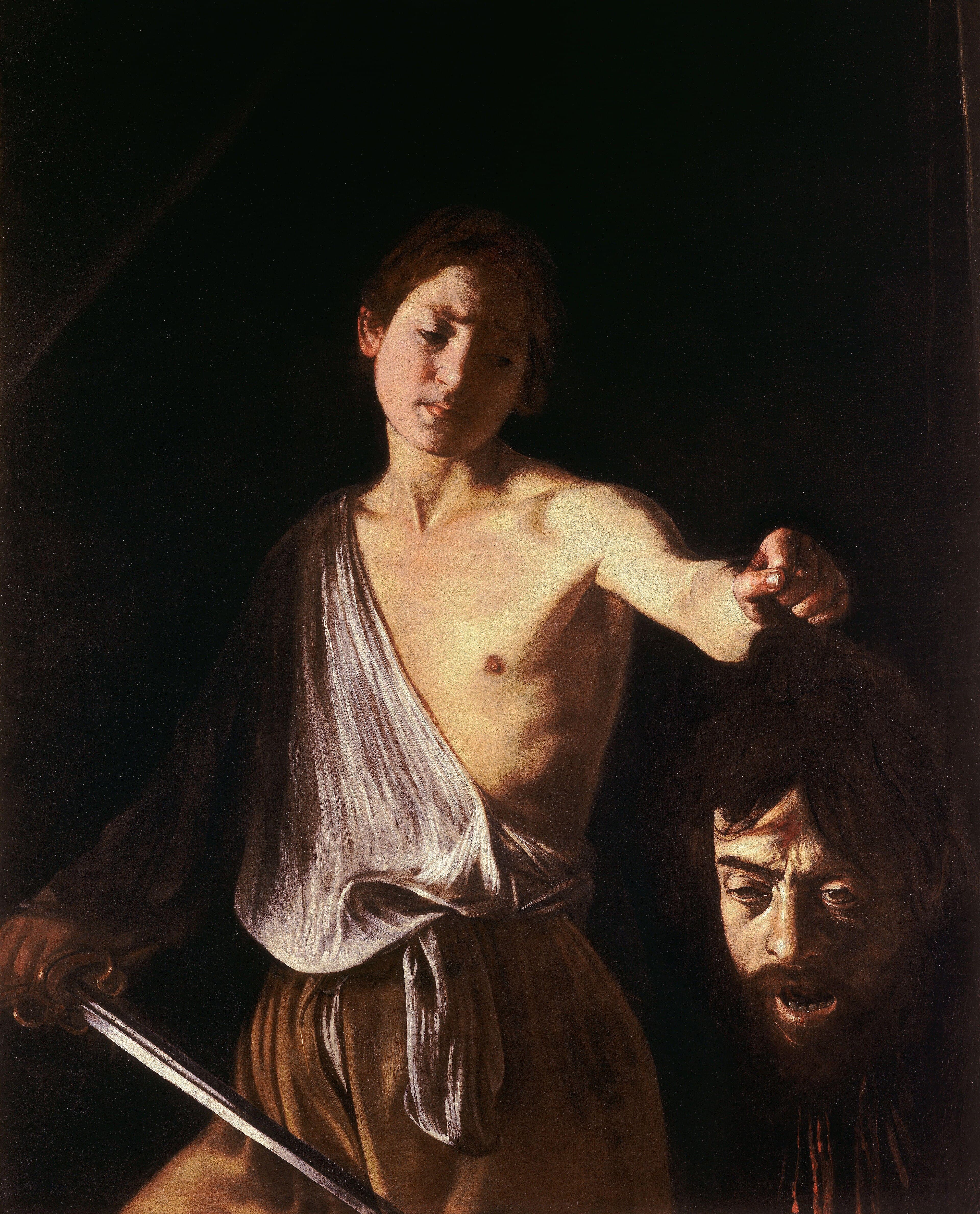A bare-shouldered boy holds out the bleeding, open-mouthed head of a bearded man against a black background — Caravaggio, David with the Head of Goliath, c. 1609–10
