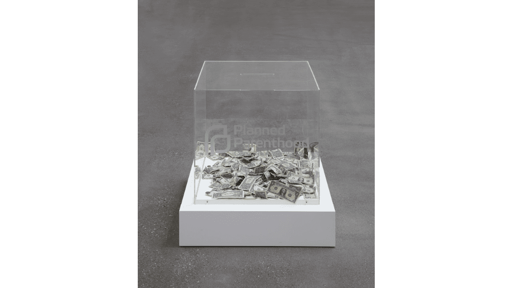 A clear acrylic cube with a Planned Parenthood logo on a white plinth, half filled with crumpled dollar bills — Jonathan Horowitz, Donation Cubes