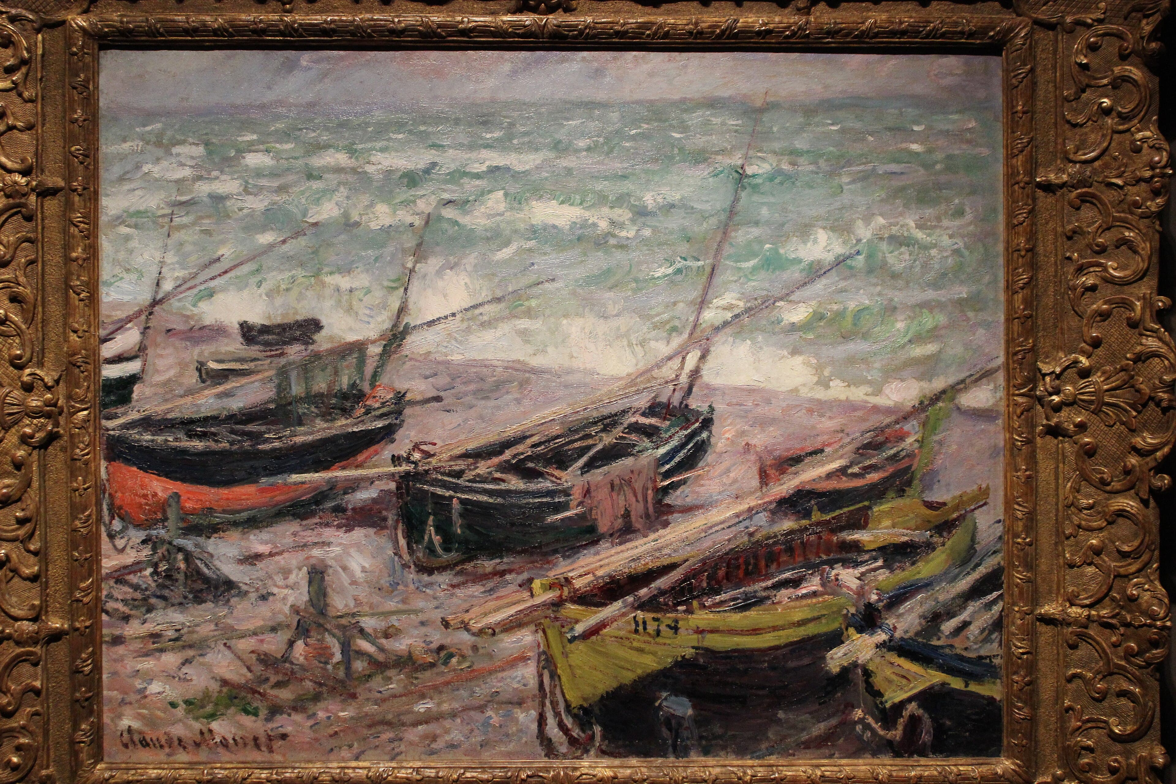 Wooden fishing boats in black, green, red and yellow lie on a pebble beach with lowered masts while green waves break in white spray behind — Claude Monet, Fishing Boats at Étretat, 1885