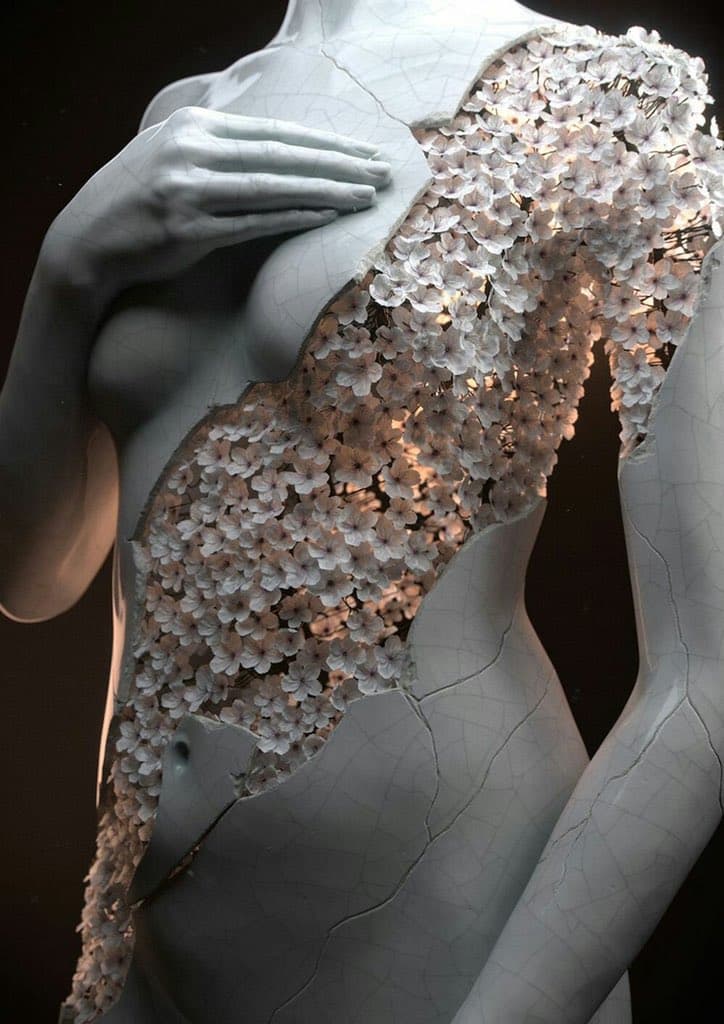 A cracked, porcelain-white female torso with one hand on the chest splits open diagonally to reveal a mass of softly glowing pale flowers — Jean-Michel Bihorel, Flower Figures Nº02, 2016