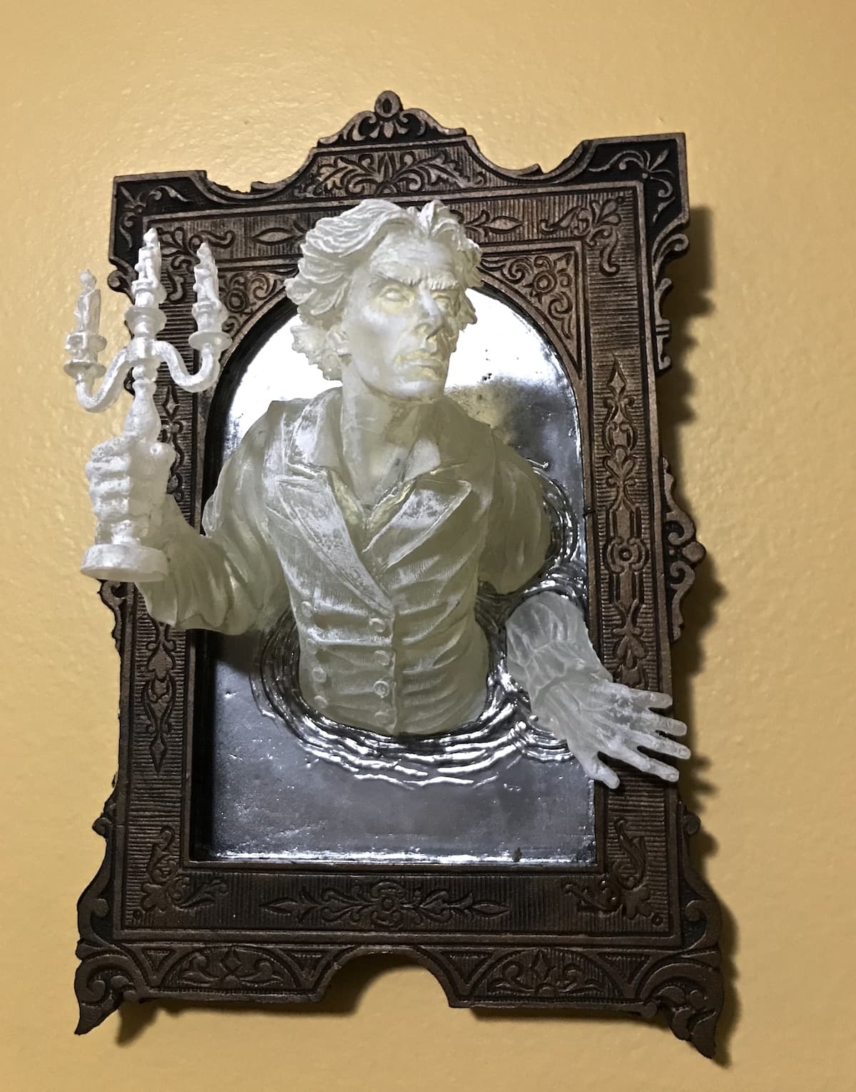A pale translucent Victorian gentleman holding a candelabrum climbs out of a rippling mirror set in an ornate dark frame — Michael Locascio, Ghost in the Mirror