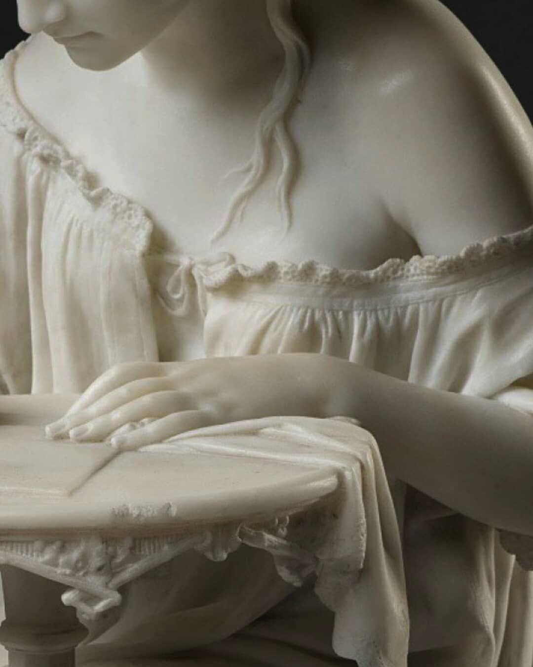 A barefoot girl in a loose nightgown slipping from one shoulder sits on a fringed stool, head bowed, writing at a small lace-covered table, all in white marble — Giovanni Spertini, Girl Writing, 1866