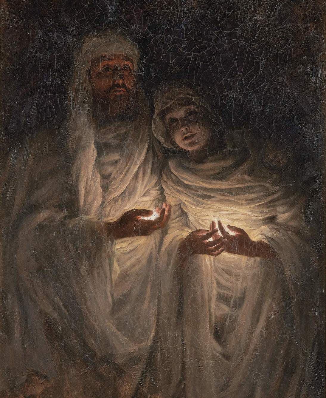 Two white-veiled figures, a bearded man and a young woman, emerge from darkness holding small glowing lights in their palms — James Tissot, The Apparition, 1885