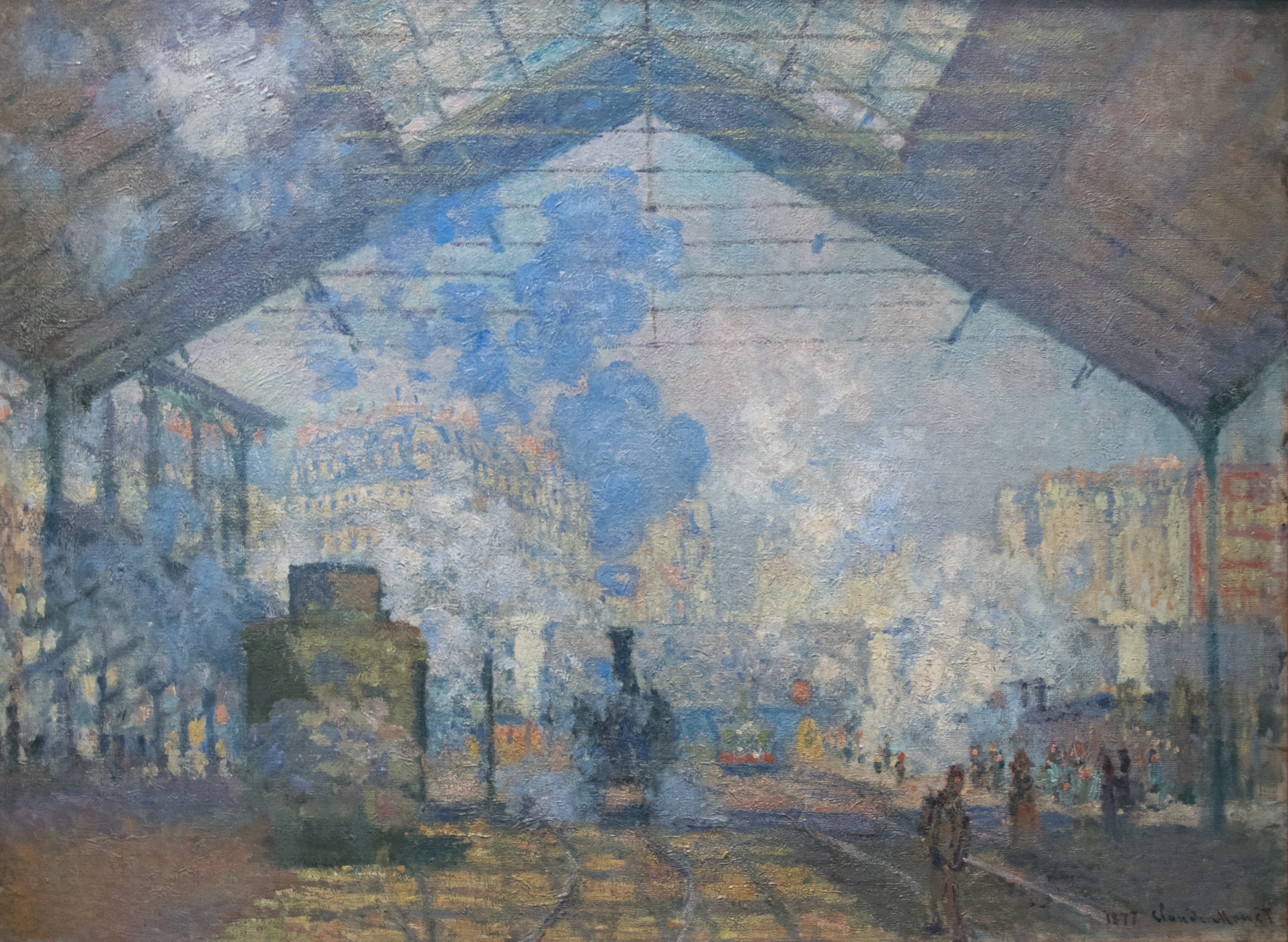 A locomotive stands under the triangular glass and iron roof of a train station while clouds of blue and white steam fill the air — Claude Monet, La Gare Saint-Lazare, 1877