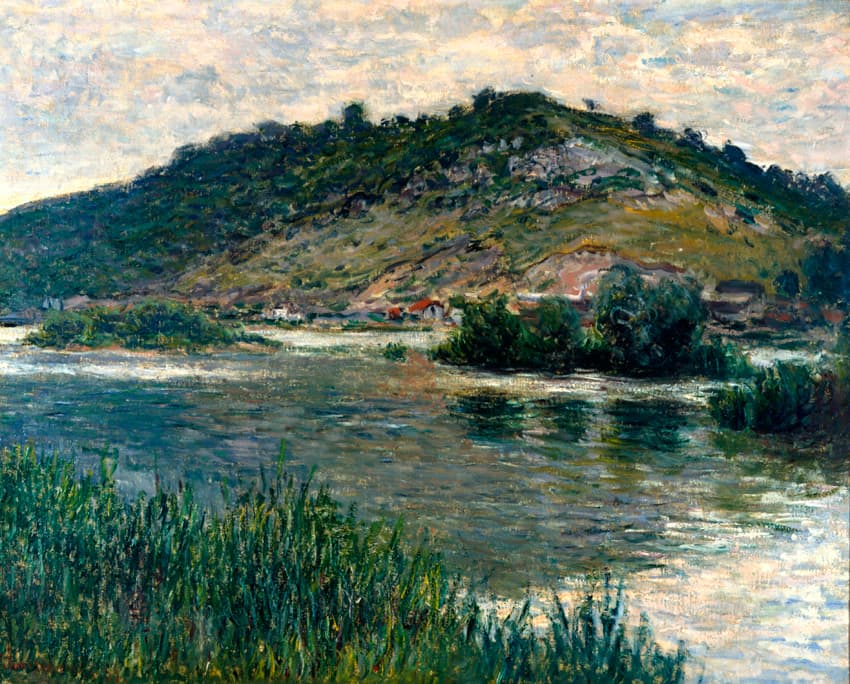 A wide river with small bushy islands flows below a steep green hill, reeds in the foreground and a pale overcast sky — Claude Monet, Landscape in Port-Villez, 1883
