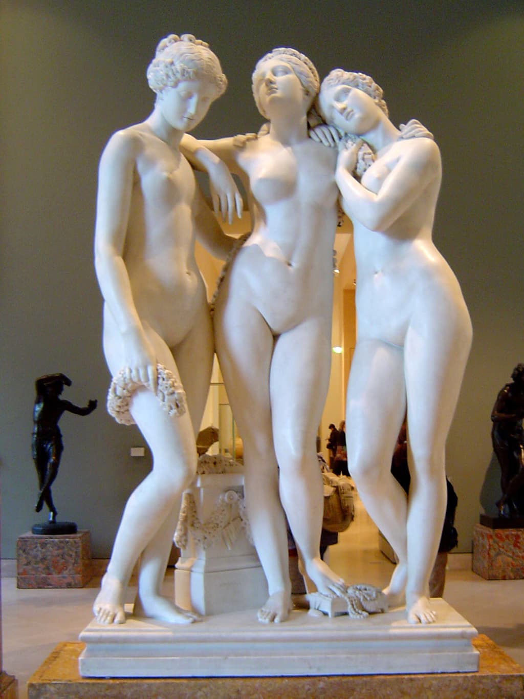 Three nude marble women stand close together, the central one with an arm over her companion's shoulder and the right one resting her head on hers — James Pradier, The Three Graces, 1831