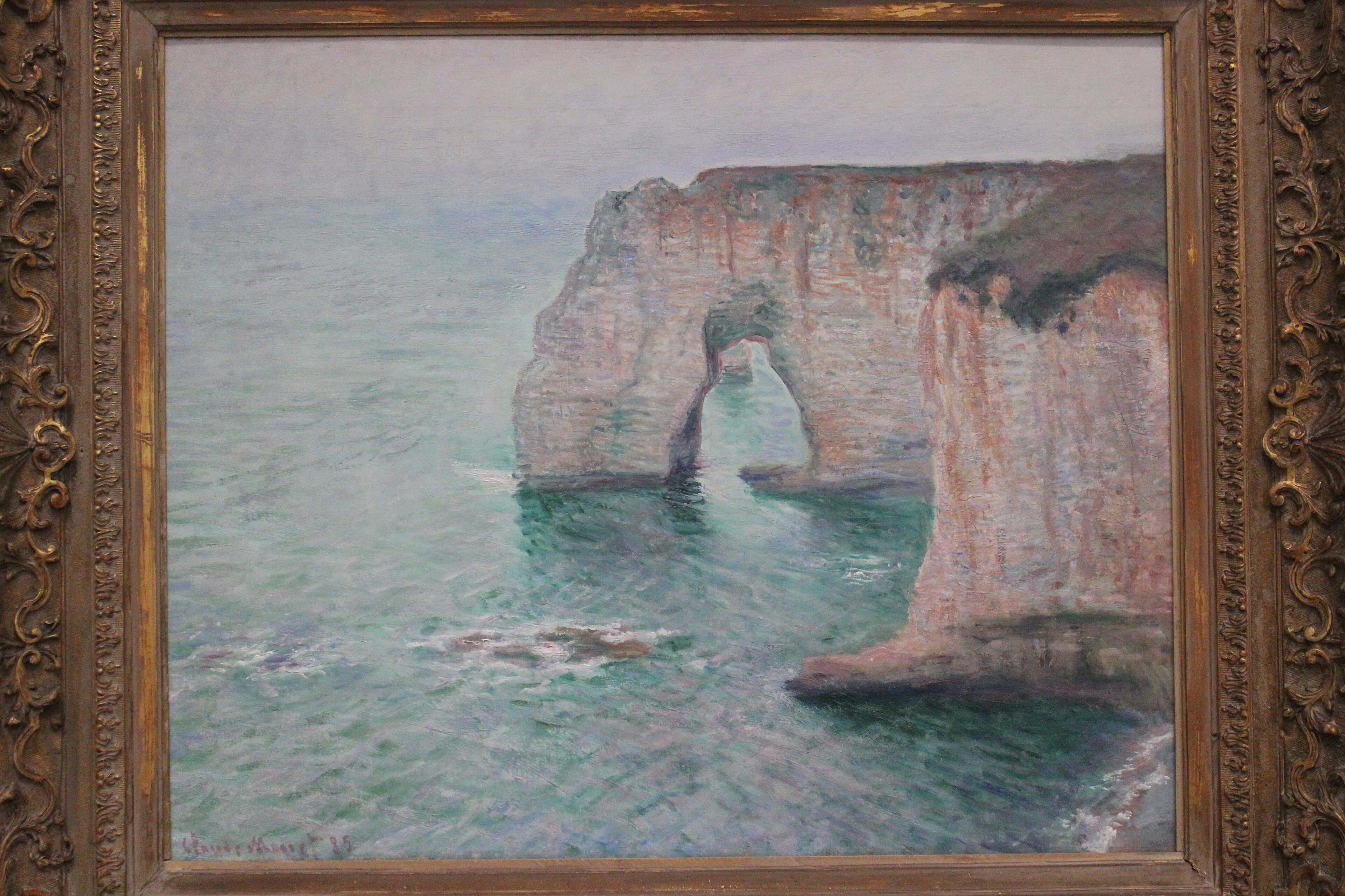 A huge pale pink chalk arch rises from a calm, milky jade sea beside a sheer cliff face under a hazy gray sky — Claude Monet, Manne-Porte, Étretat, 1885