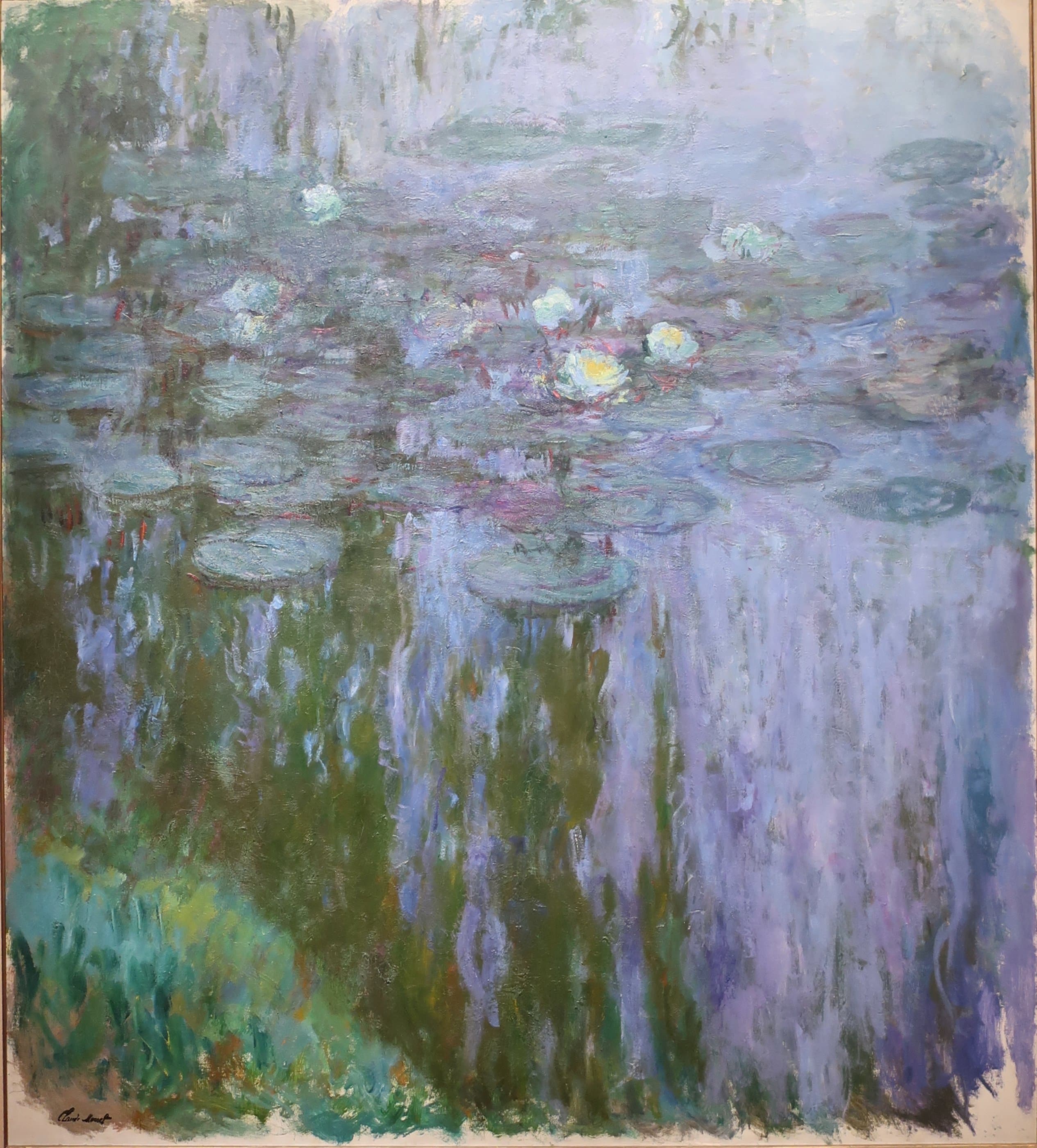 White and yellow lilies on blue-grey pads above a lilac cascade of willow reflection, with a green grassy bank at lower left — Claude Monet, Nymphéas, 1916–19