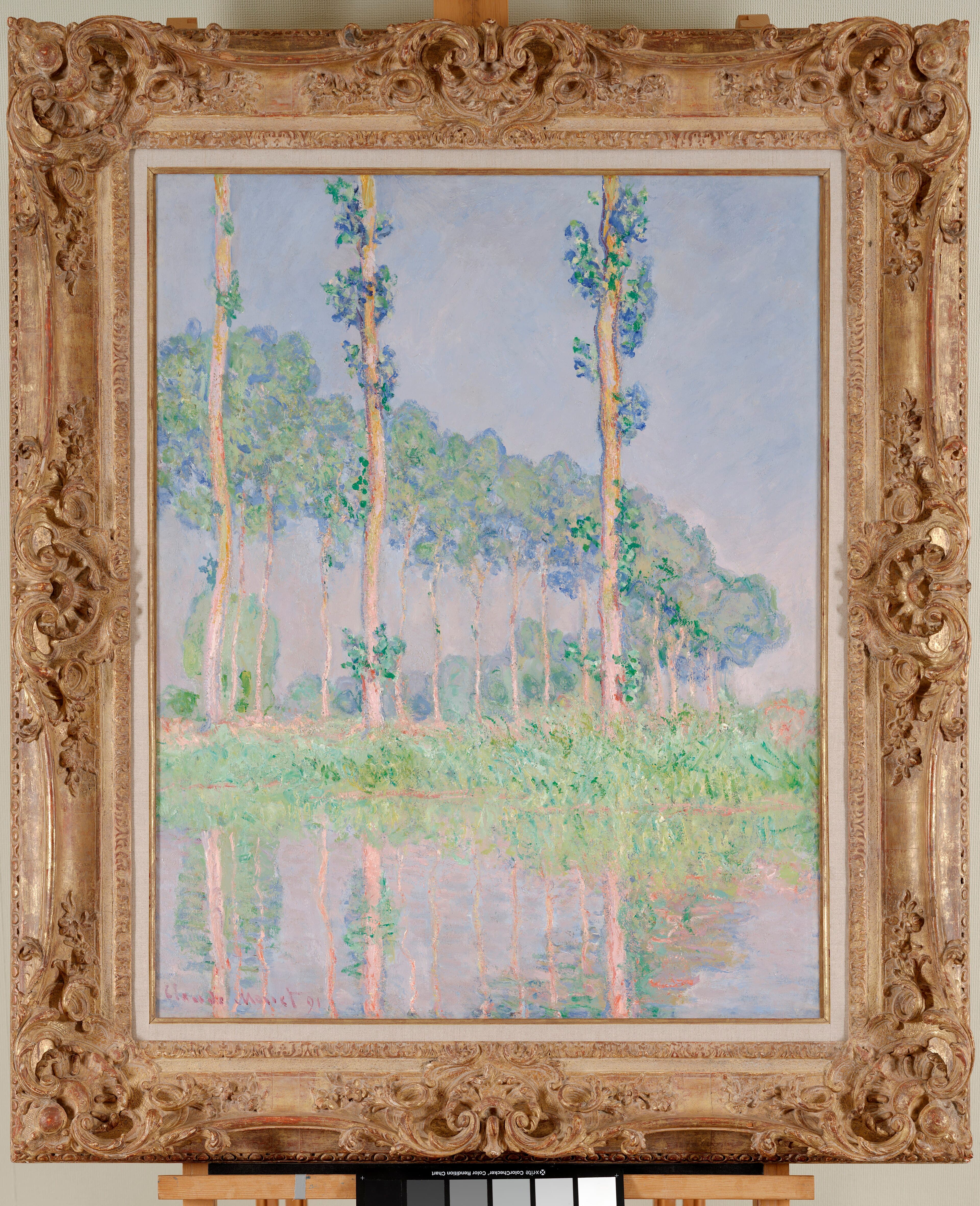 Three slender poplar trunks with tufts of green leaves stand before a curving row of pale trees under a lilac sky, reflected in pink water — Claude Monet, Poplars, Pink Effect, 1891