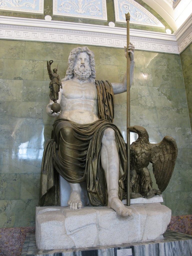 A colossal bearded god sits enthroned with bare marble torso and bronze-colored drapery, holding a scepter and a small Victory, an eagle at his feet — Statue of Jupiter, Roman, late 1st century AD, State Hermitage Museum