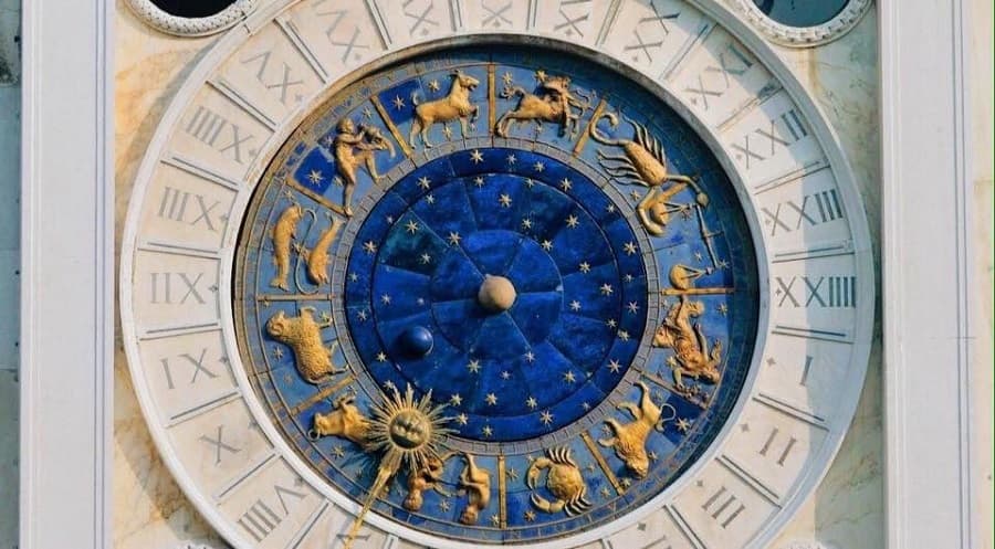 A blue enamel clock face with gilded zodiac signs, gold stars and a sun pointer inside a marble ring of Roman numerals I to XXIV — St Mark's Clocktower, Venice, 1496–99