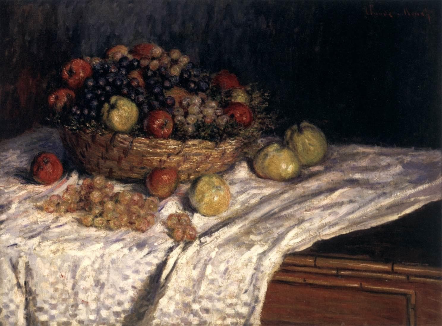 A wicker basket heaped with red apples and dark and pale grapes sits on a white cloth draped over a wooden table, with loose fruit around it — Claude Monet, Apples and Grapes, 1879–80