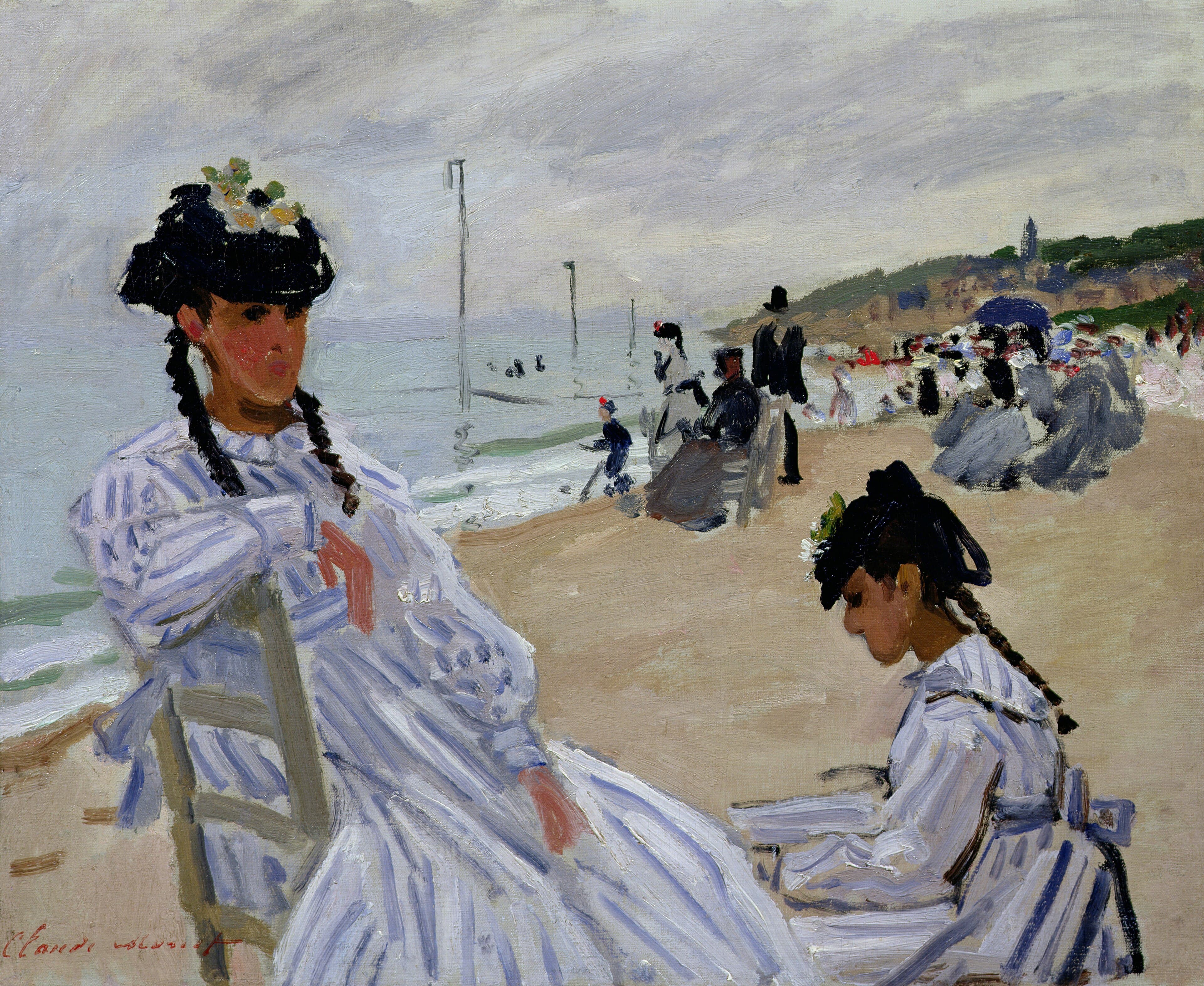 A young woman in a blue-and-white striped dress and flowered hat sits on a beach chair beside another woman bent over her lap, with beach crowds and sea behind — Claude Monet, On the Beach at Trouville, 1870