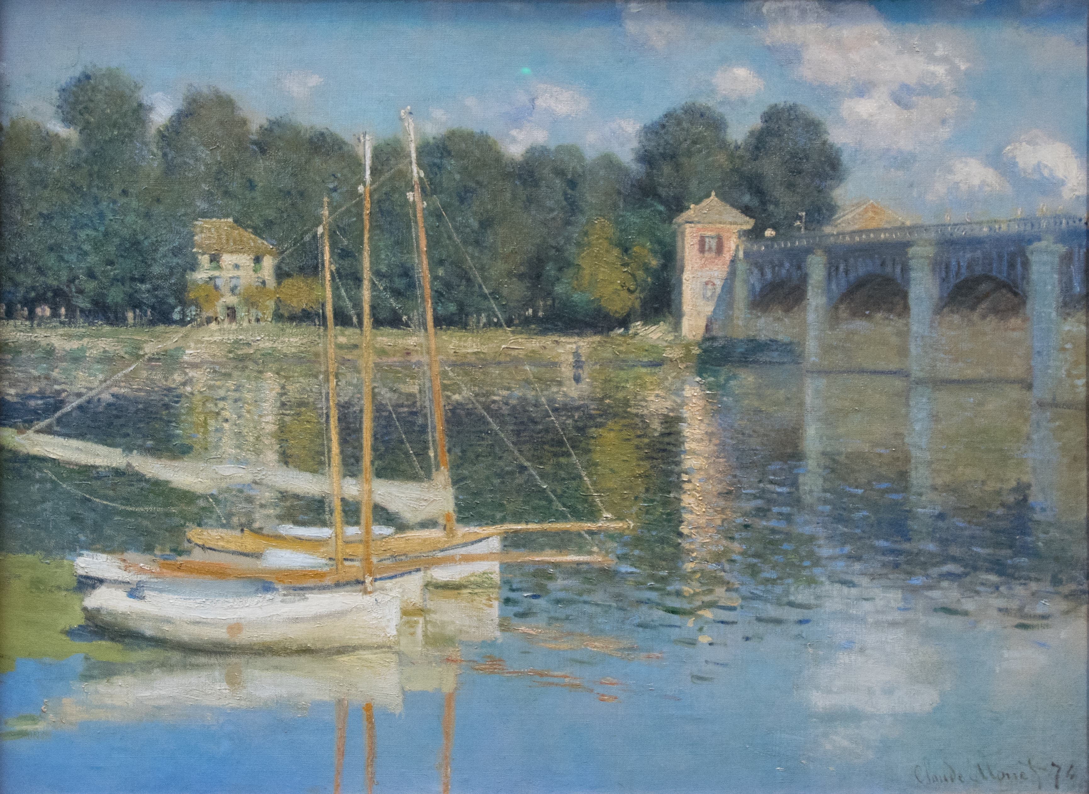 Two white sailboats with bare masts moored in blue water before an arched stone bridge and a small pink tollhouse — Claude Monet, The Argenteuil Bridge, 1874
