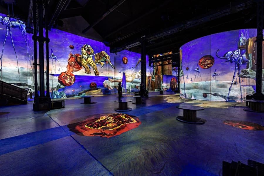 Projections of Dalí's long-legged elephants, a leaping tiger and dreamlike plains cover the walls of a vast dark industrial hall — Dalí, l'énigme sans fin, Atelier des Lumières, 2021