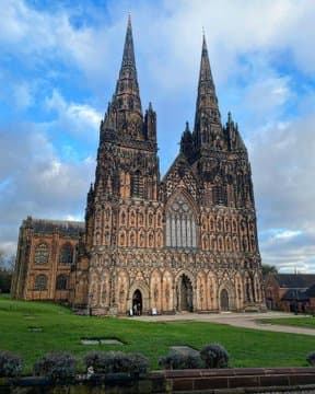The red sandstone west front of a Gothic cathedral with two tall spires and tiers of statues in niches under a blue sky — Lichfield Cathedral, Staffordshire, c. 1195–1340