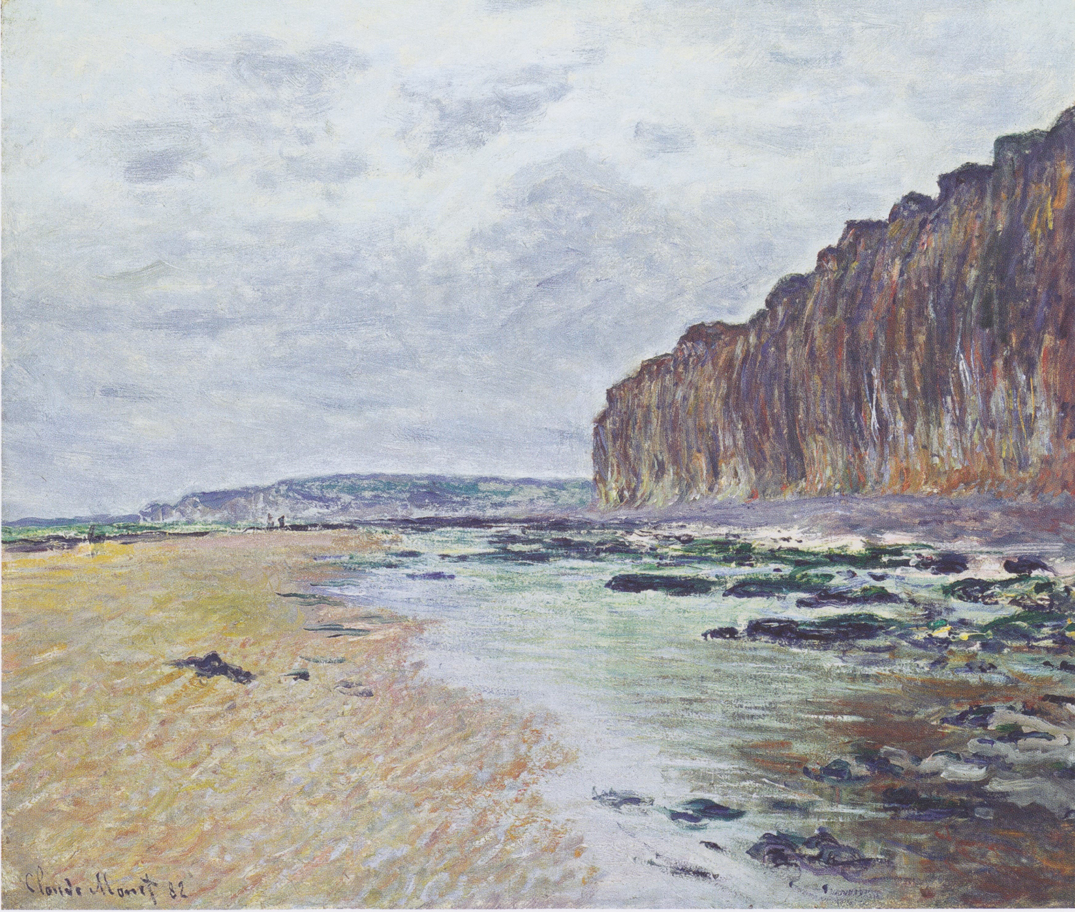 A wide beach at low tide, golden wet sand and seaweed-covered rocks beneath a towering rust-colored chalk cliff at right under a cloudy sky — Claude Monet, Varengeville, Low Tide, 1882