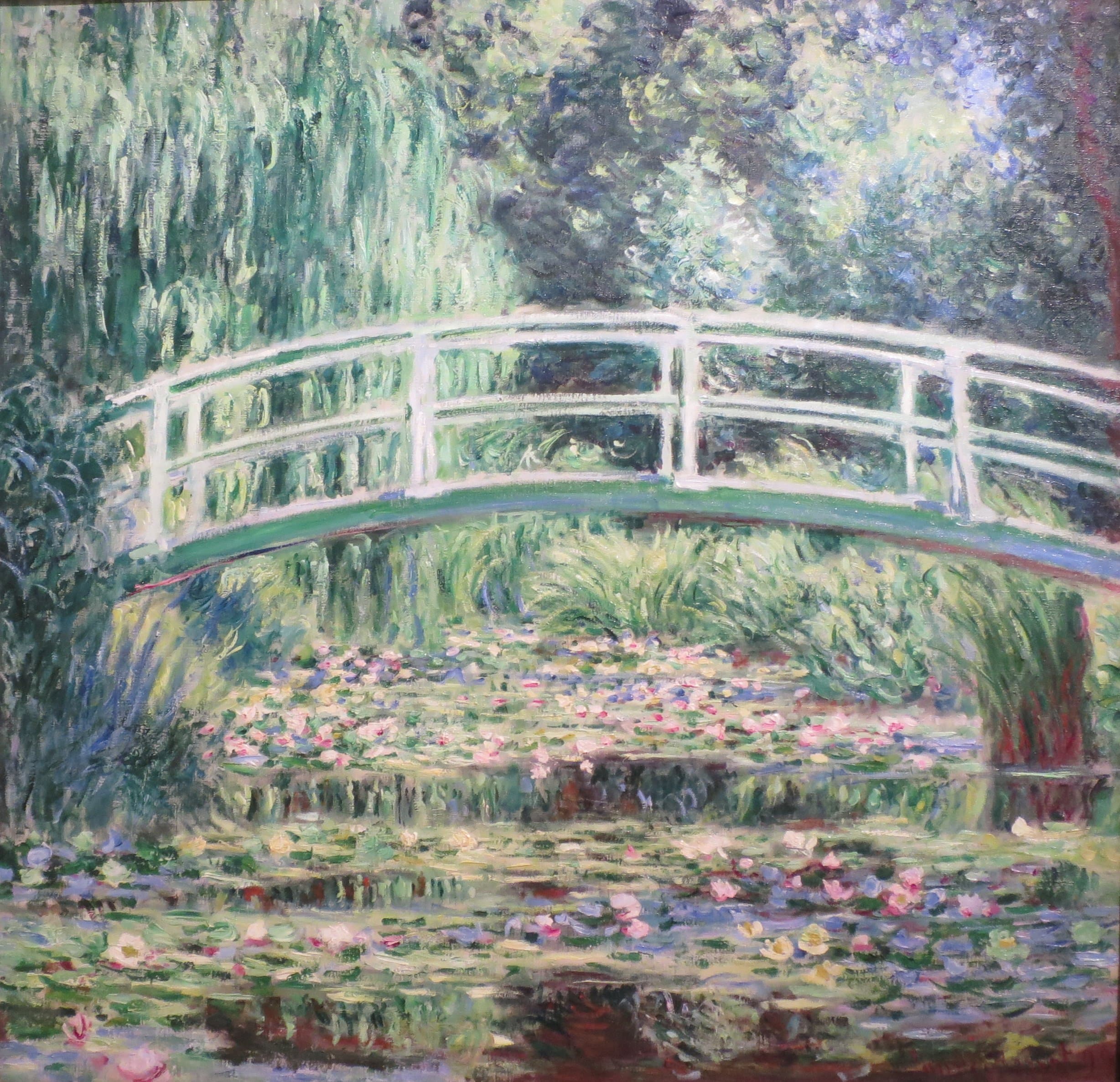 A pale arched footbridge spans a pond crowded with lily pads and white and pink flowers, a willow and dense trees behind — Claude Monet, White Water Lilies, 1899
