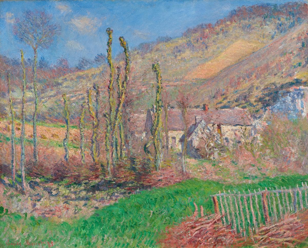 A row of thin pollarded trees stands before a farmhouse at the foot of a sunlit pink and ocher hillside, with green grass and a wooden fence in front — Claude Monet, Winter Landscape at the Val de Falaise, 1885